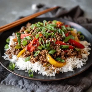 A plate of ground beef stir fry with bell peppers and green beans over brown rice, garnished with sesame seeds.